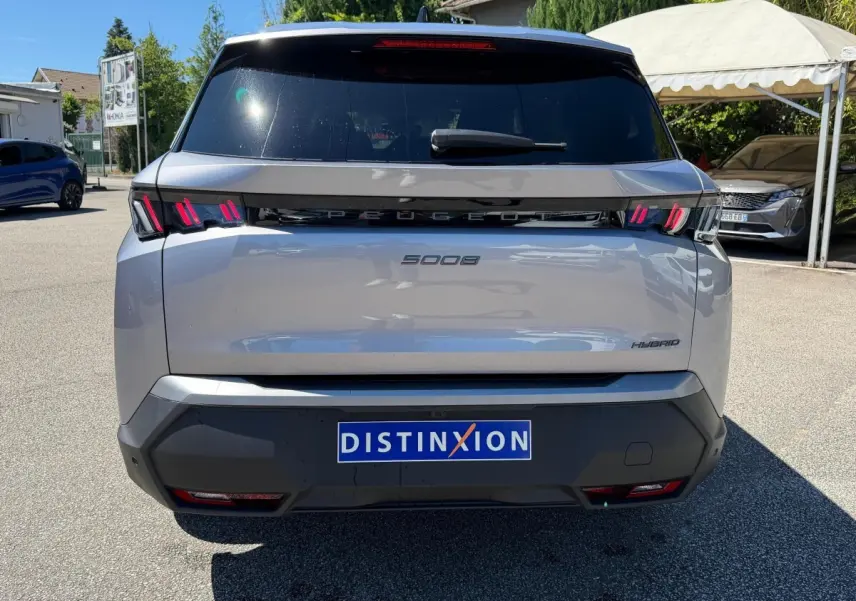 Vue arrière d’un Peugeot 5008 gris clair hybride, avec feux LED distinctifs et logo Peugeot noir brillant.
