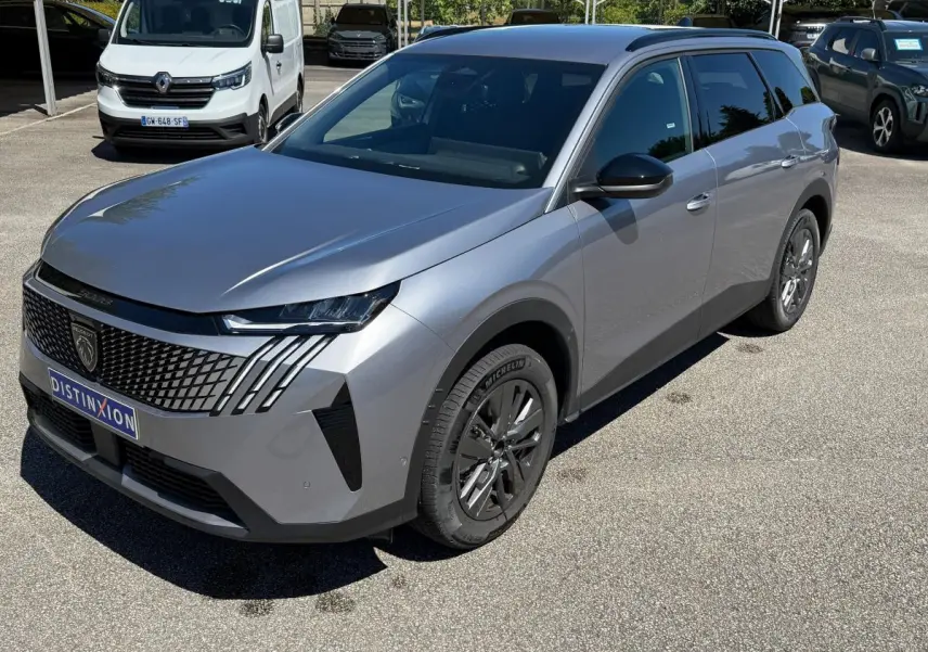 Vue 3/4 avant droit d’un Peugeot 5008 gris clair avec calandre noire et jantes foncées sur parking extérieur.