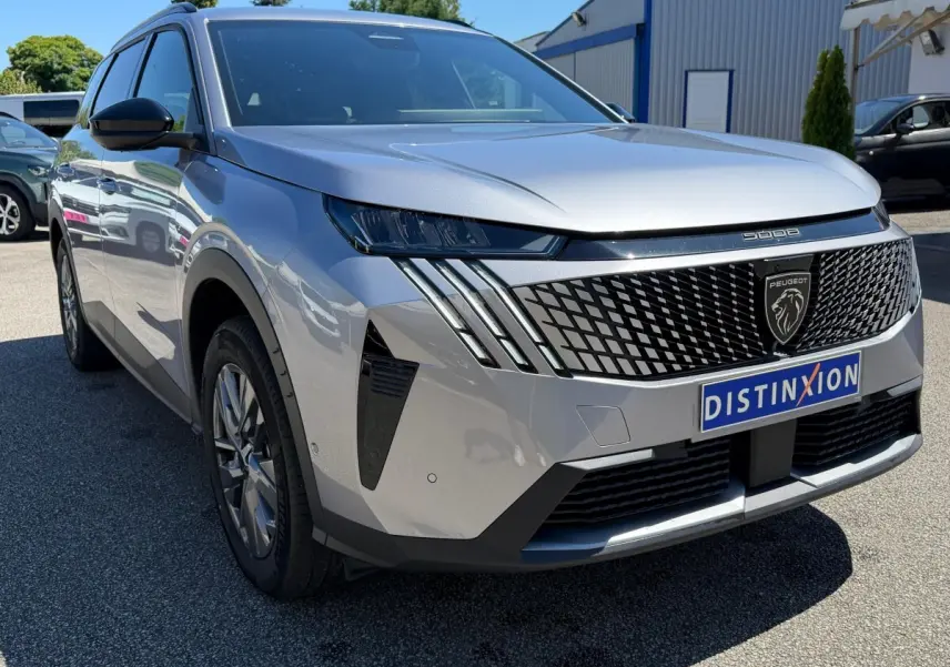 Peugeot 5008 gris clair vue 3/4 avant avec calandre noire à motif géométrique et feux LED distinctifs.