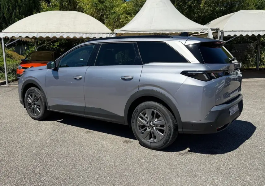 Peugeot 5008 gris clair vue 3/4 arrière droit, SUV hybride avec vitres arrière teintées et jantes foncées.