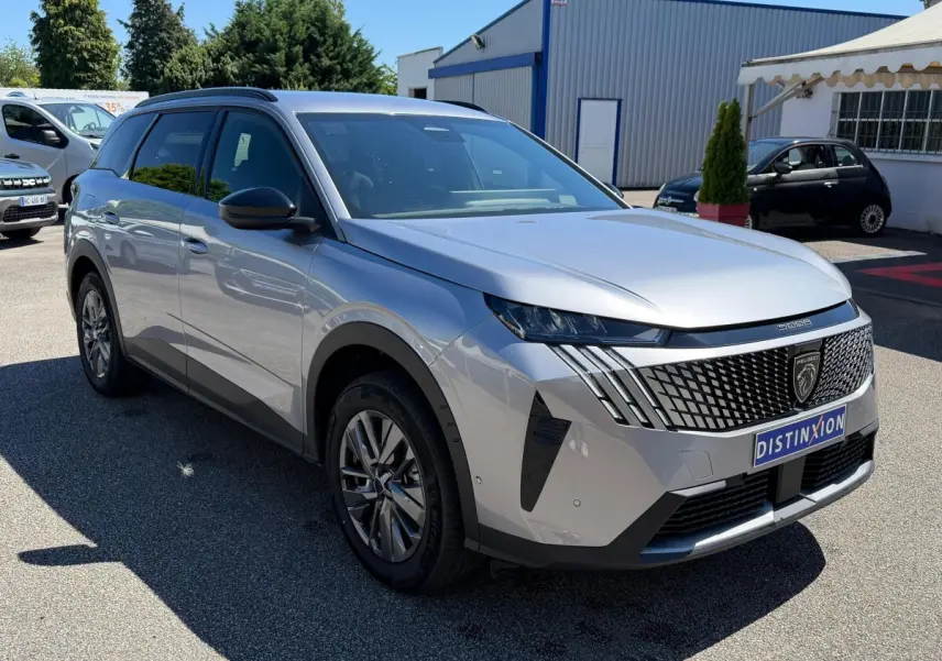 Peugeot 5008 gris clair vue 3/4 avant droit, avec calandre distinctive et phares LED en journée.