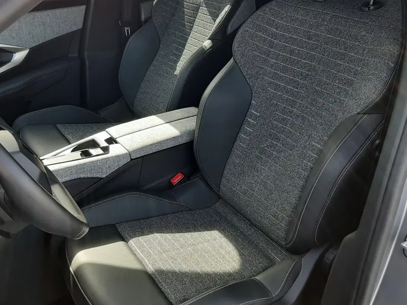 Vue intérieure côté conducteur du Peugeot 5008 gris clair 2025, sièges tissu et cuir avec console centrale assortie.