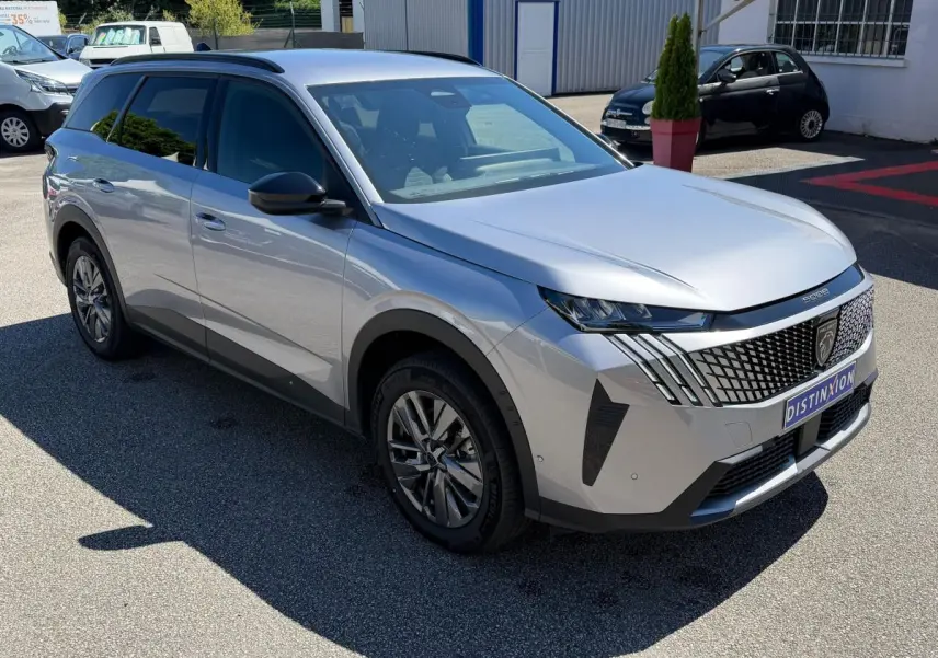 Peugeot 5008 gris clair vue 3/4 avant, avec calandre distinctive et feux LED effilés, stationné en extérieur.