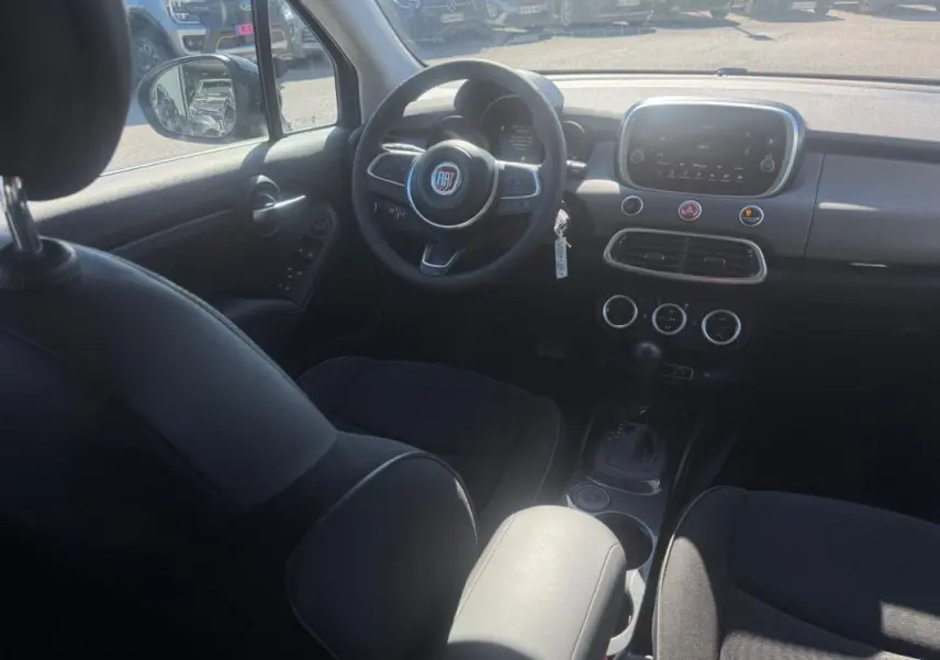 Vue intérieure avant du tableau de bord et volant du Fiat 500X MY23 avec écran tactile et commandes au volant.