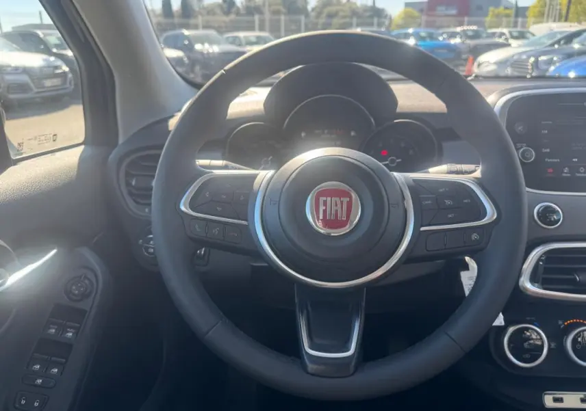 Vue intérieure centrée sur le volant noir avec logo FIAT, tableau de bord et commandes de la Fiat 500X bleu 2024.