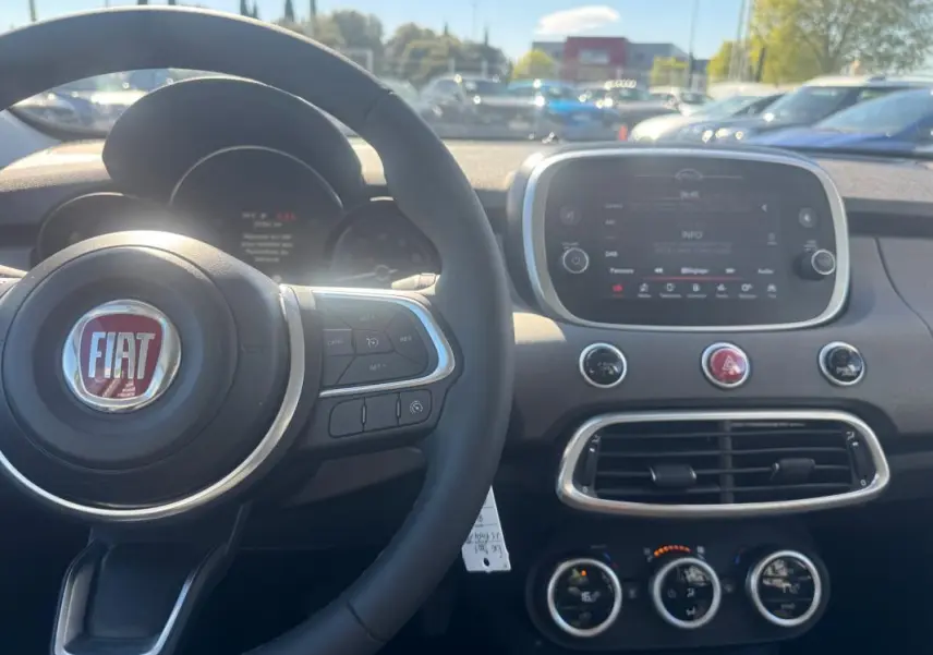 Vue intérieure du tableau de bord de la Fiat 500X bleu MY23, avec volant, écran tactile et commandes de climatisation visibles.