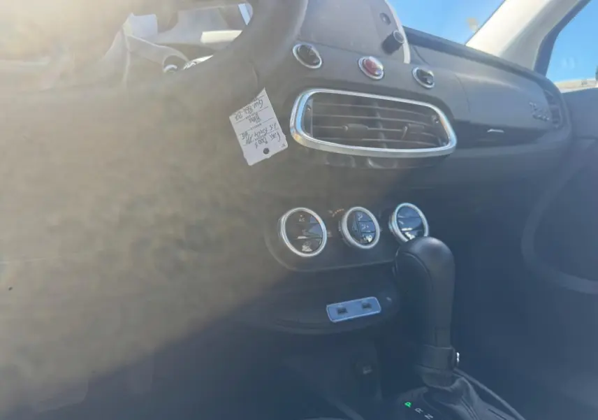 Vue intérieure de la console centrale et levier de vitesse de la Fiat 500X MY23, avec commandes de climatisation et volant partiel visible.