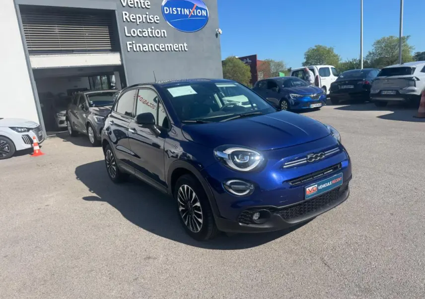 Fiat 500X bleu vue 3/4 avant droit, avec jantes 16 pouces classiques et phares ronds allumés.