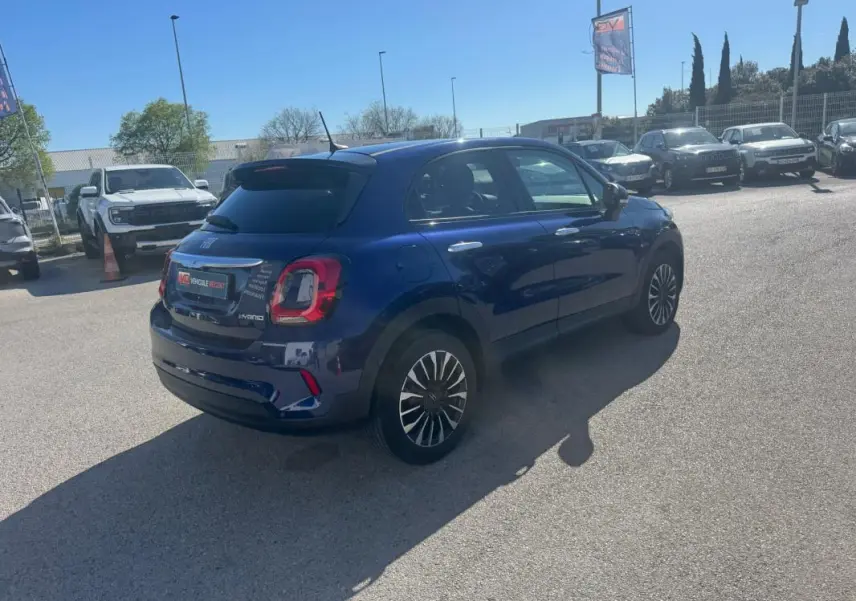 Vue 3/4 arrière droite d'une FIAT 500X bleu foncé avec jantes classiques 16 pouces, stationnée en extérieur.