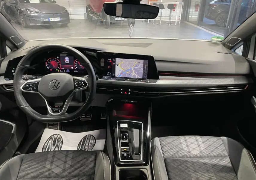Vue intérieure avant de la Volkswagen Golf VIII R-Line blanche, tableau de bord avec écran tactile et volant multifonctions cuir.