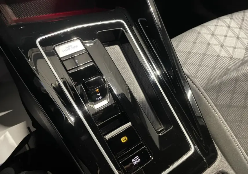 Gros plan sur la console centrale noire brillante avec levier de vitesses automatique et bouton start/stop, siège tissu gris à motifs.