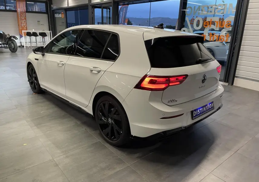 Volkswagen Golf 1.5 eTSI 2024 blanc vue 3/4 arrière droit avec jantes noires et vitres teintées.