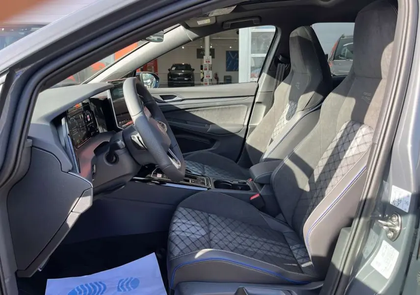 Vue intérieure côté conducteur de la Volkswagen Golf gris dauphin, sièges sport R-Line en tissu et alcantara avec surpiqûres bleues.