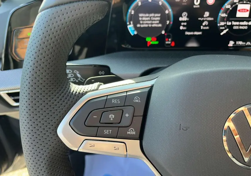 Gros plan sur le volant cuir multifonctions côté gauche de la Volkswagen Golf gris dauphin avec tableau de bord numérique.