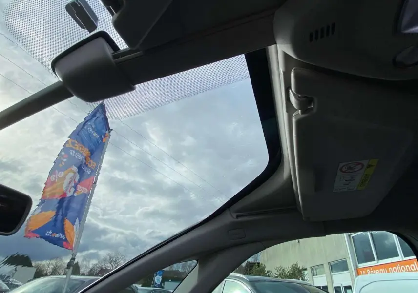 Vue intérieure du toit ouvrant panoramique du Citroën Grand C4 Picasso blanc, avec pare-soleil et ciel nuageux visible.