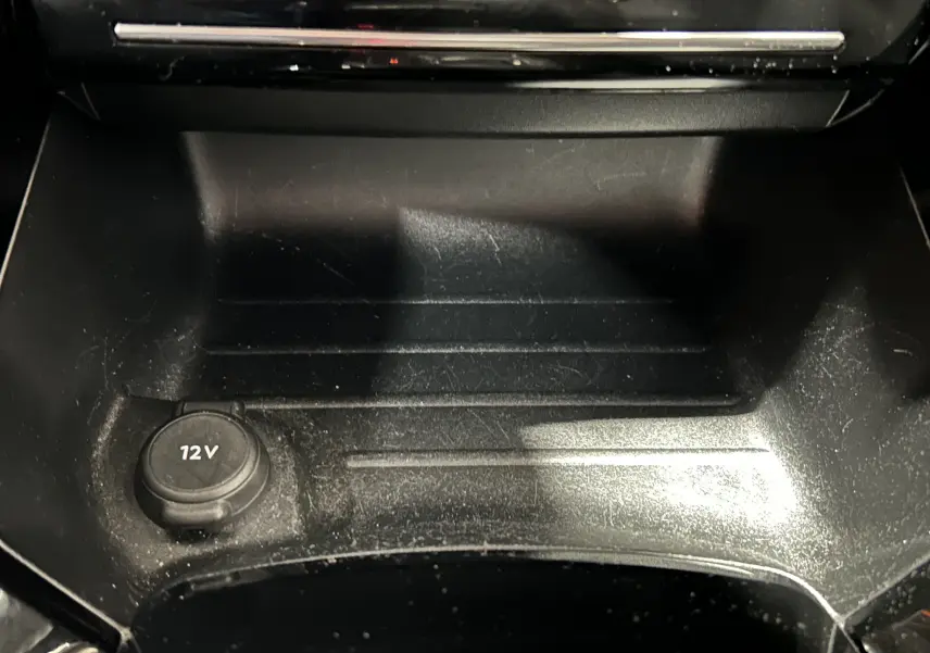 Gros plan sur la prise 12V dans le rangement central noir de l'intérieur du Peugeot 2008 Gris Artense 2023.