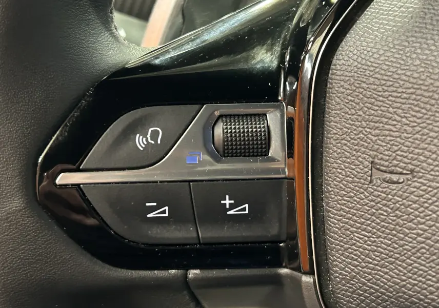 Gros plan sur les commandes noires du volant côté gauche d’un Peugeot 2008 gris Artense, avec boutons de volume et commande vocale.
