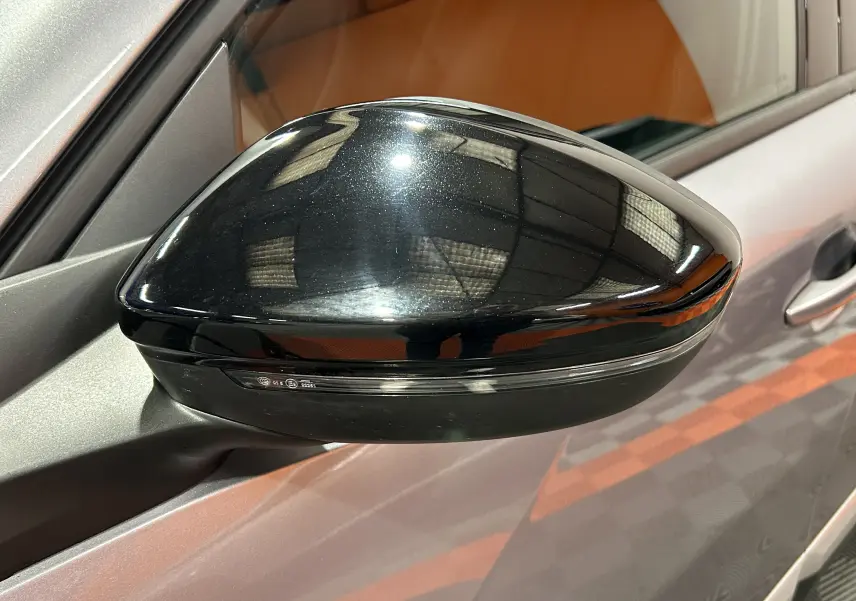 Rétroviseur noir brillant côté gauche d’un Peugeot 2008 gris Artense, vue rapprochée sur la portière avant.