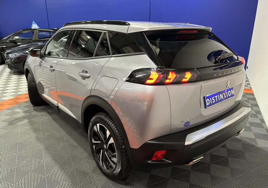 Vue 3/4 arrière droite d'un Peugeot 2008 gris Artense avec feux arrière allumés et jantes noires bicolores.