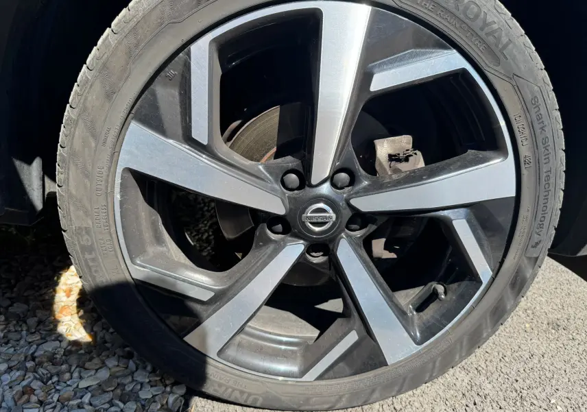 Gros plan sur la jante alu noire et grise du Nissan Qashqai II PH2, avec logo Nissan au centre.