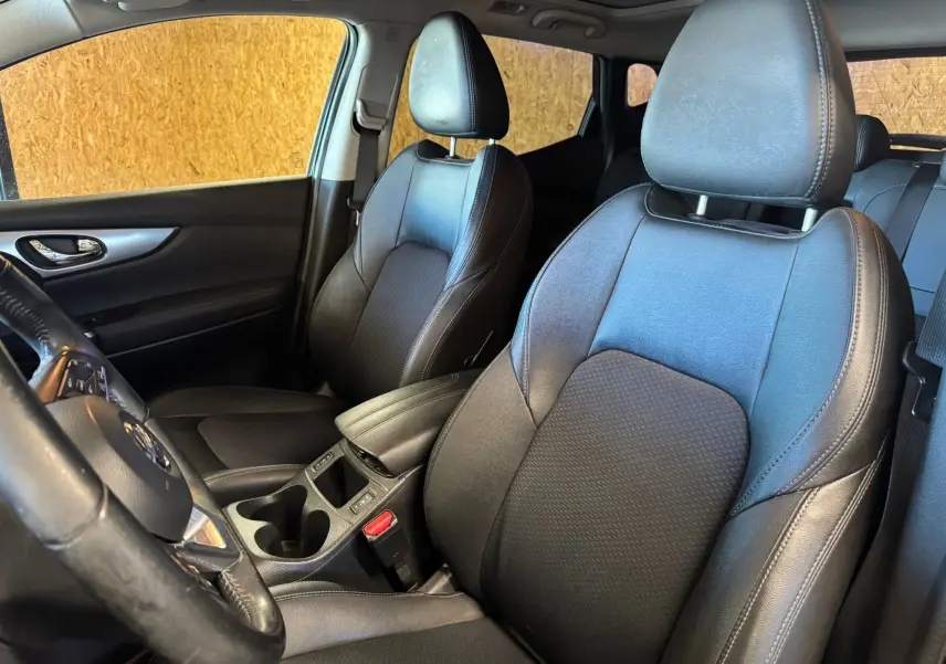 Vue intérieure côté conducteur du Nissan Qashqai noir, mettant en valeur les sièges en cuir noir et l'accoudoir central.