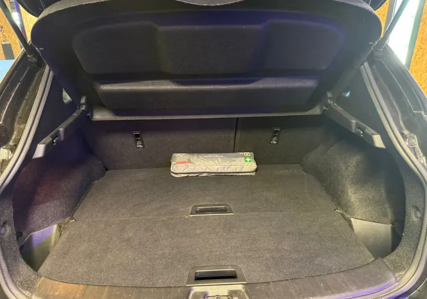 Vue intérieure du coffre ouvert d'un Nissan Qashqai noir, avec un kit de secours Nissan posé à l'arrière.
