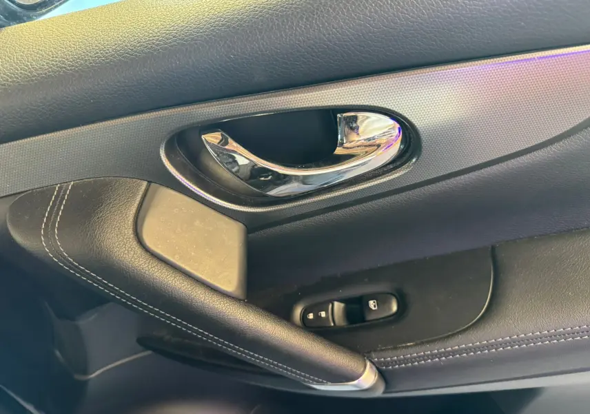 Poignée de porte intérieure côté conducteur du Nissan Qashqai noir, avec commandes de vitres et finition cuir noir.