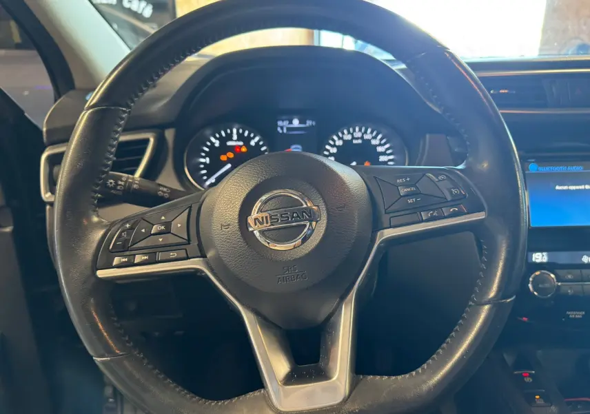 Vue rapprochée du volant cuir multifonctions noir du Nissan Qashqai II PH2 avec tableau de bord et écran tactile en arrière-plan.