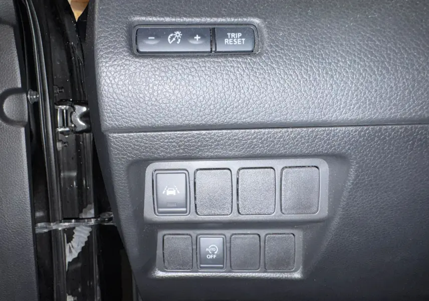 Gros plan sur les commandes de sécurité et réglages du tableau de bord du Nissan Qashqai II PH2 noir, côté conducteur.