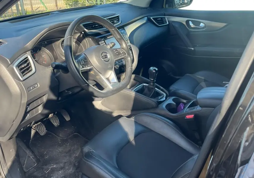 Vue 3/4 arrière droite du Nissan Qashqai noir avec jantes alu et barres de toit, stationné en intérieur lumineux.