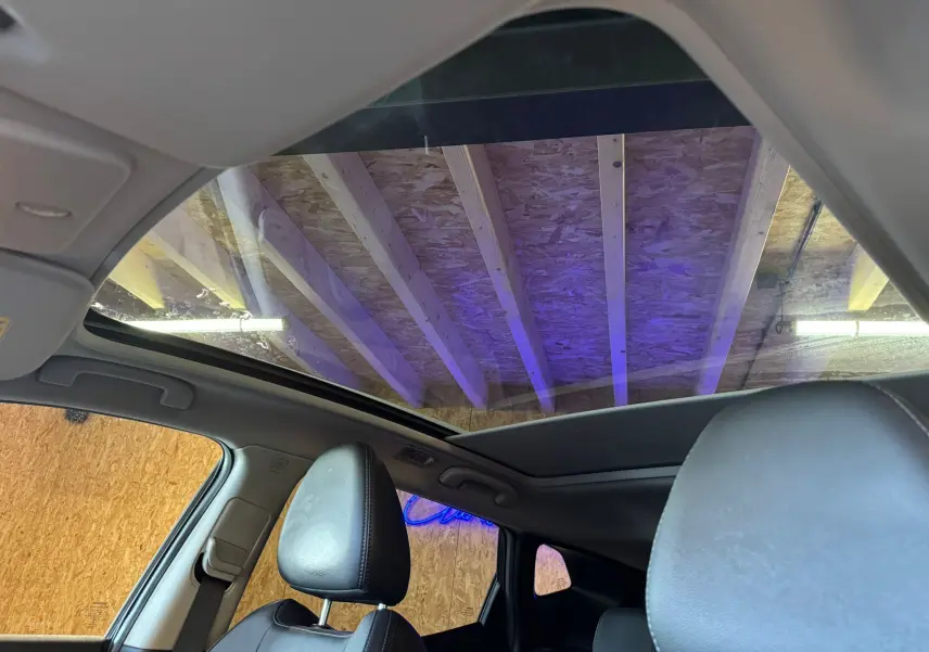 Vue intérieure du Nissan Qashqai noir montrant le toit panoramique et les sièges avant en cuir noir.