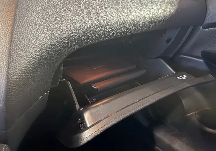 Gros plan sur la boîte à gants ouverte côté passager du Nissan Qashqai II PH2 noir, montrant un livret à l'intérieur.