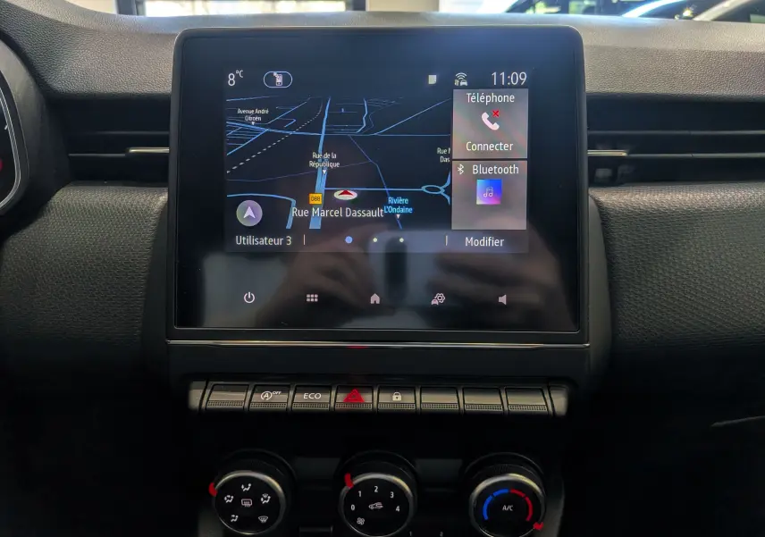 Vue rapprochée de l'écran tactile central et des commandes de climatisation d'une Renault Clio V blanche.