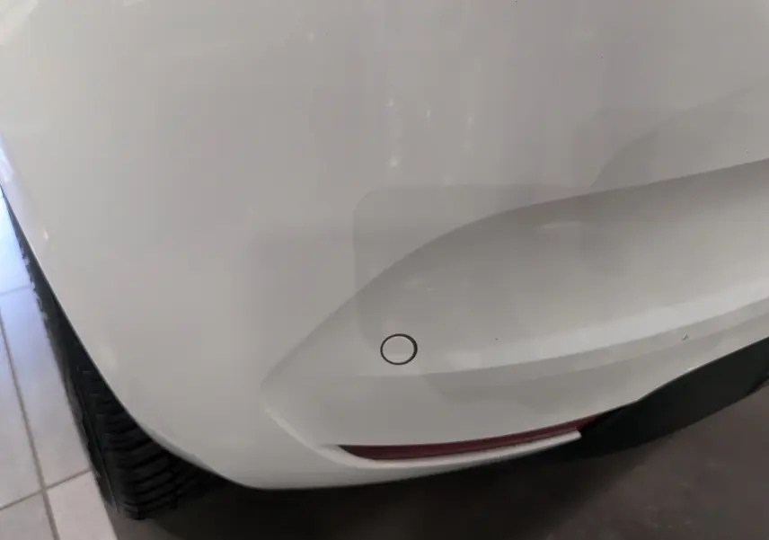 Gros plan sur l'angle arrière droit blanc glacier d'une Renault Clio V Business 2020 avec capteur de stationnement visible.