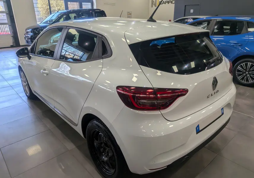 Vue 3/4 arrière droite d'une Renault Clio V Business blanc glacier en intérieur, avec feux arrière LED et jantes noires.