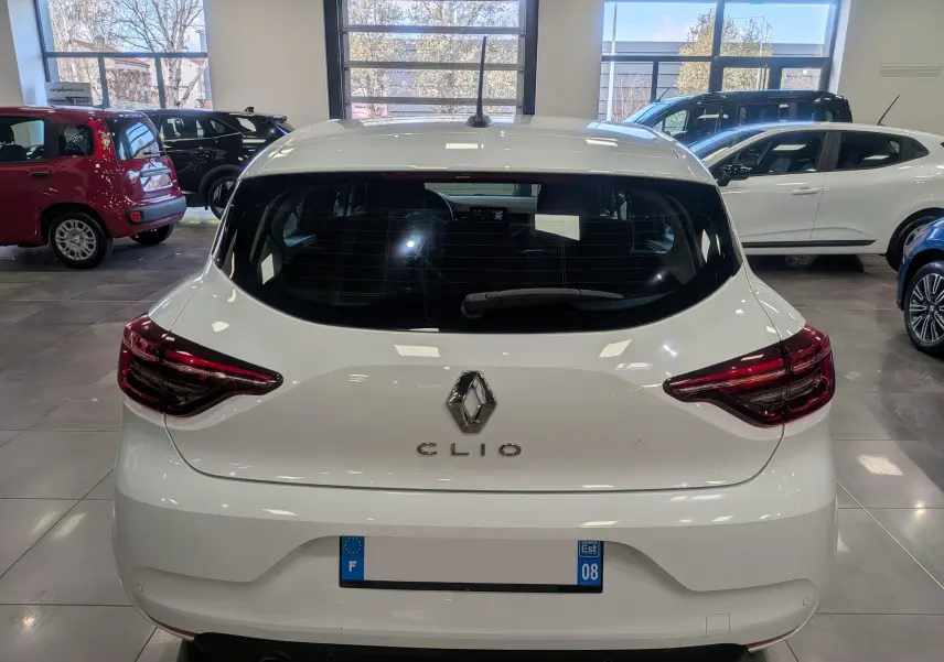 Vue arrière d'une Renault Clio V Blanc Glacier en showroom, avec feux arrière LED et logo centré visible.