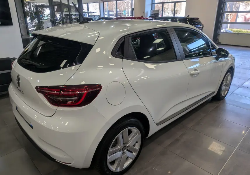 Vue 3/4 arrière droite d'une Renault Clio V Business blanc glacier en showroom, soulignant ses feux arrière LED et jantes alliage.