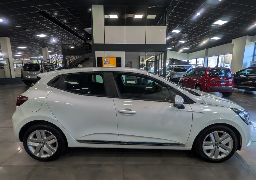 Profil côté gauche d'une Renault Clio V Business blanc glacier, en intérieur de showroom avec jantes alliage visibles.