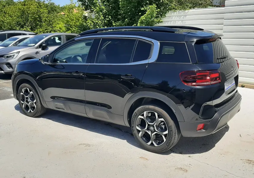 Vue 3/4 arrière droite d'un Citroën C5 Aircross noir Perla Nera avec jantes distinctives et barres de toit visibles.