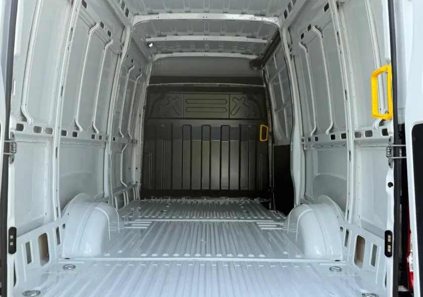 Vue intérieure arrière du fourgon Iveco Daily blanc 2026, montrant l'espace de chargement vide avec poignées jaunes.