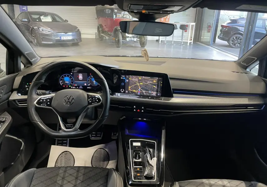 Vue intérieure avant de la Volkswagen Golf VIII R-Line noire, tableau de bord avec écran tactile et volant multifonctions cuir.