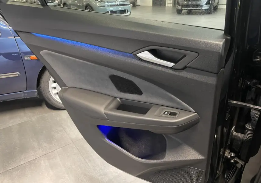 Vue intérieure de la porte arrière droite noire métallisée de la Volkswagen Golf 1.5 eTSI VIII R-Line avec éclairage d’ambiance bleu.