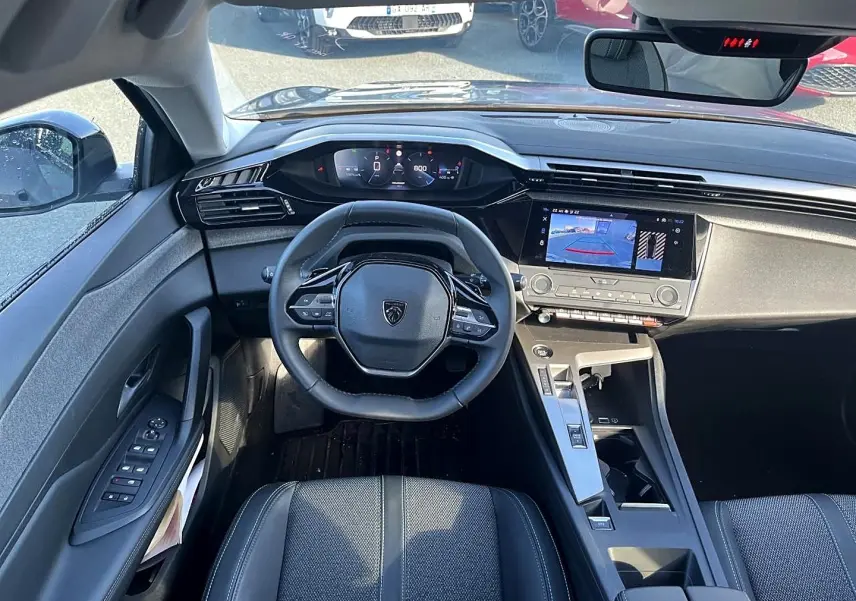 Intérieur de la Peugeot 308 2025 vue de face, tableau de bord noir avec écran tactile et volant compact multifonction.