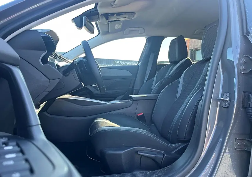Intérieur avant droit d’une Peugeot 308 gris selenium, sièges tissu noir avec surpiqûres claires et accoudoir central.
