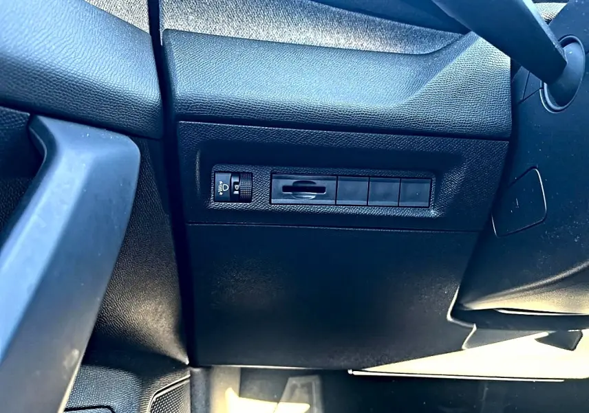 Détail intérieur côté gauche montrant les commandes d'éclairage et la texture noire du tableau de bord du Peugeot 308 gris selenium.