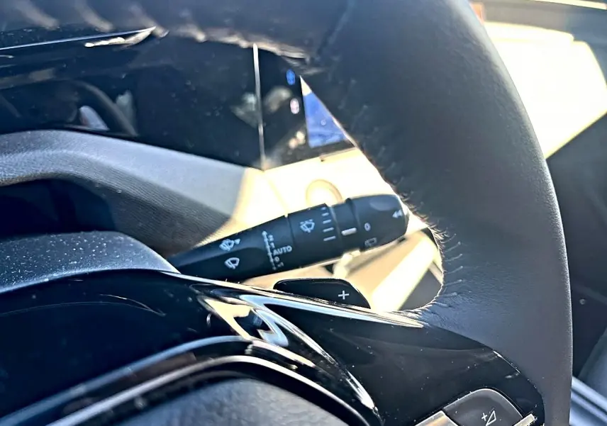 Gros plan sur le volant noir de la Peugeot 308 2025 avec commandes intégrées et manette d'essuie-glace visible en arrière-plan.