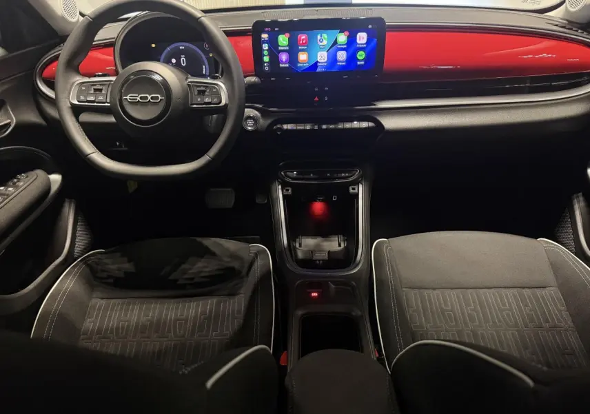 Vue intérieure avant de la Fiat 600 2025, tableau de bord rouge foncé avec écran tactile et volant noir marqué 600.