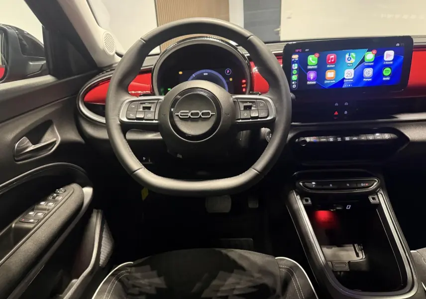 Vue intérieure frontale du poste de conduite du Fiat 600 rouge foncé avec volant multifonction et écran tactile large.