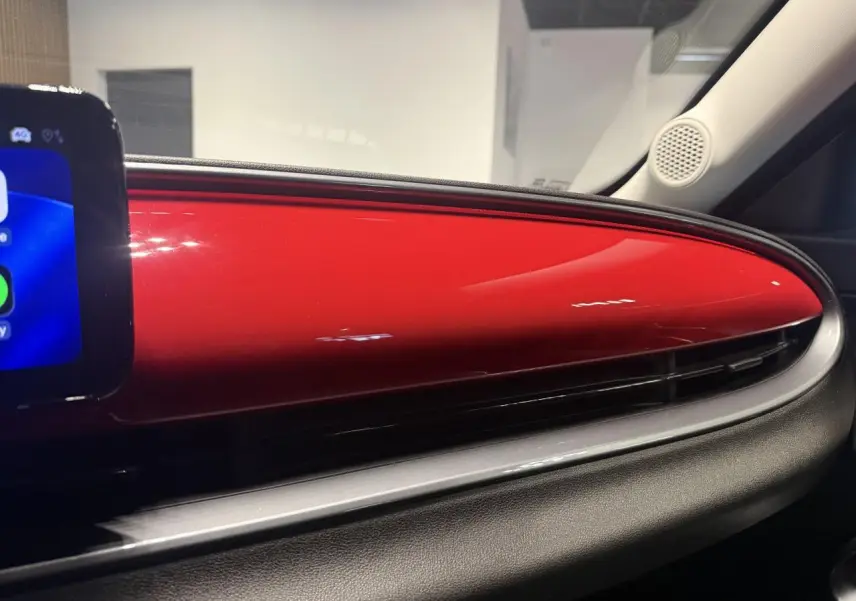 Détail intérieur du tableau de bord rouge foncé de la FIAT 600 Hybrid 2025 avec écran tactile partiel visible à gauche.