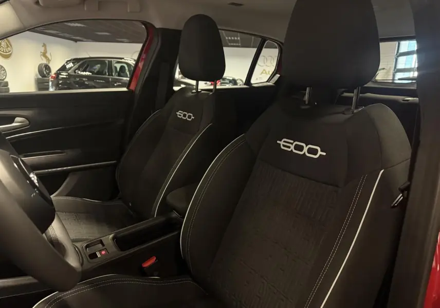Vue intérieure des sièges avant noirs avec logo 600 brodé, dans une FIAT 600 rouge foncé.